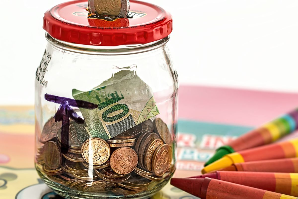 Pote de vidro com moedas e uma nota, ao lado de gizes de cera